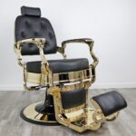 barber shop chairs Knockout Gold barber chair featuring matte black vinyl upholstery, a gold-chromed steel frame, tufted backrest buttons, and a heavy-duty hydraulic base.
